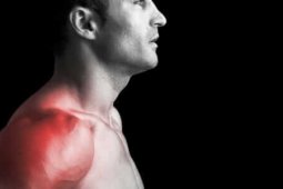Muscular man suffering with shoulder pain on black background